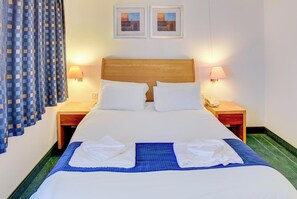Una habitación de hotel con una cama, dos mesitas de noche, una lámpara, un teléfono y una cortina a cuadros.