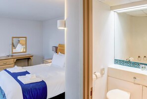 Une chambre d’hôtel comprenant un lit, un bureau, un miroir, une salle de bain avec des toilettes et un lavabo.