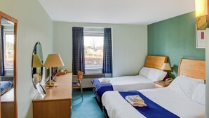 Une chambre d’hôtel avec deux lits, un bureau avec des lampes, une chaise et une fenêtre avec des rideaux.