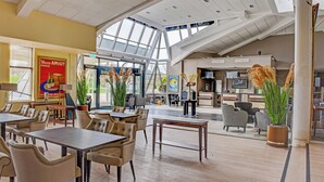 Un vaste espace intérieur doté de hauts plafonds, de grandes fenêtres et de différents types de mobilier, notamment des tables et des chaises.
