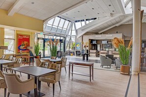 Un espacio interior amplio con techos altos, ventanas grandes y diversas opciones de mobiliario, incluyendo mesas y sillas.