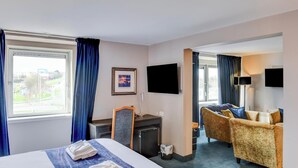 Une chambre d’hôtel avec un lit, un bureau, une télévision et deux fauteuils.