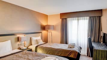 Habitación de hotel con dos camas, un escritorio, una silla, una lámpara y un ventanal grande con cortinas.