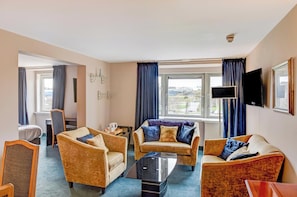 Habitación de hotel con sofá, televisor de pantalla plana, ventana con cortinas y vista a la ciudad.