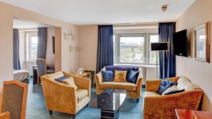 Une chambre d’hôtel équipée d’un canapé, d’un téléviseur à écran plat, d’une fenêtre avec des rideaux et offrant une vue sur la ville.