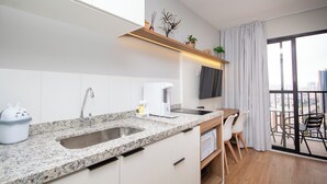 Une cuisine moderne dotée de plans de travail en granit, d’un évier encastré et d’une machine à café. On y trouve également un coin repas avec une table et des chaises, ainsi qu’une grande fenêtre offrant une vue sur la ville.