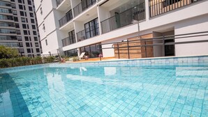Une piscine dont le fond est recouvert de carrelage, entourée d’un bâtiment blanc doté de balcons et de fenêtres.