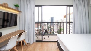 Une chambre d’hôtel moderne dotée d’un balcon, d’un téléviseur à écran plat, d’un bureau en bois, de chaises blanches et d’un lit.