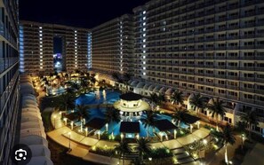 A multi-story hotel with a swimming pool surrounded by palm trees and outdoor lighting. - Idyllic Apartment for Rent - Perfect for Short-term Stay Front of Mall of Asia (Pasay)