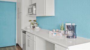 A modern kitchen with white cabinetry, a microwave, a coffee maker, and a potted plant.