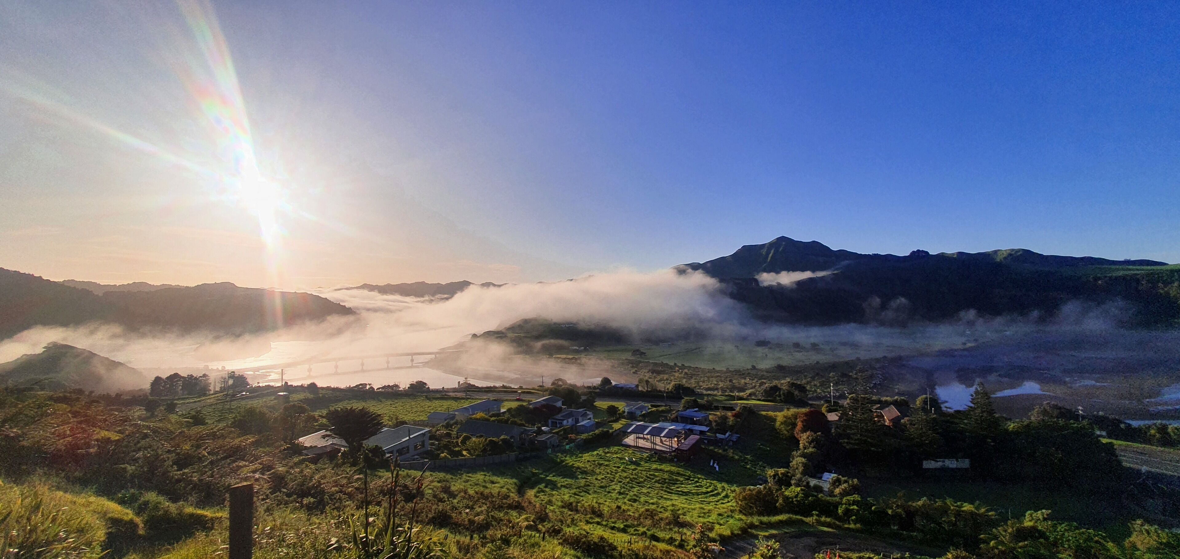 A mountainous landscape with a bridge, houses, and greenery.