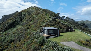 A modern house on a hillside with a small deck and a hot tub. - Rustic Mokau Escape with Ocean Views & Sauna (Mokau)