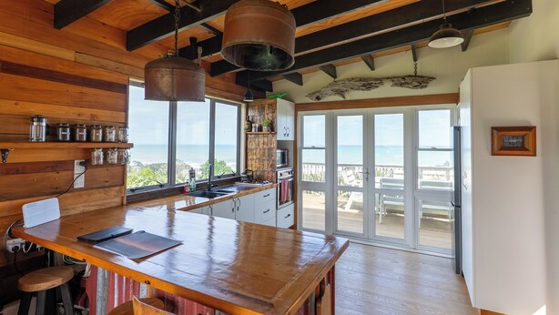 A kitchen with wooden beams, a large island, and a view of the ocean. - Rustic Mokau Escape with Ocean Views & Sauna (Mokau)