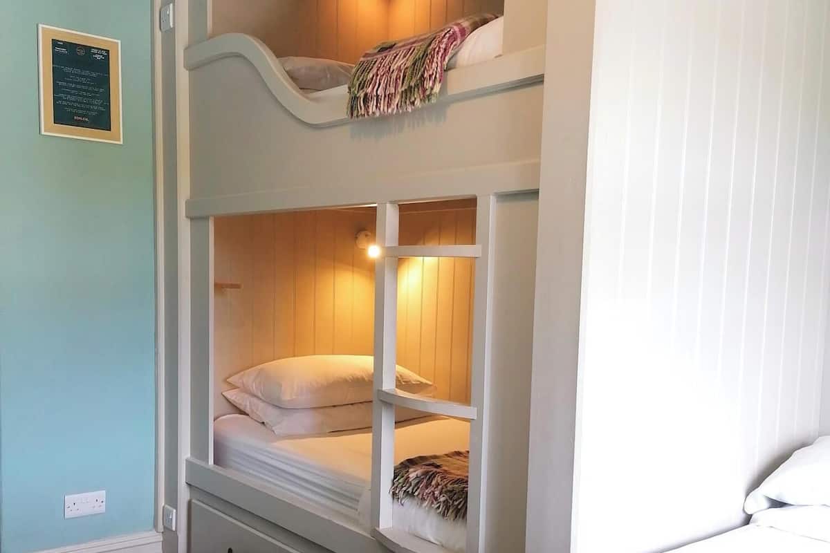 A bunk bed room with a lower bunk and a single bed, a small bedside table, and a wall-mounted light fixture.