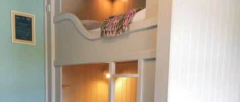 A bunk bed room with a lower bunk and a single bed, a small bedside table, and a wall-mounted light fixture.