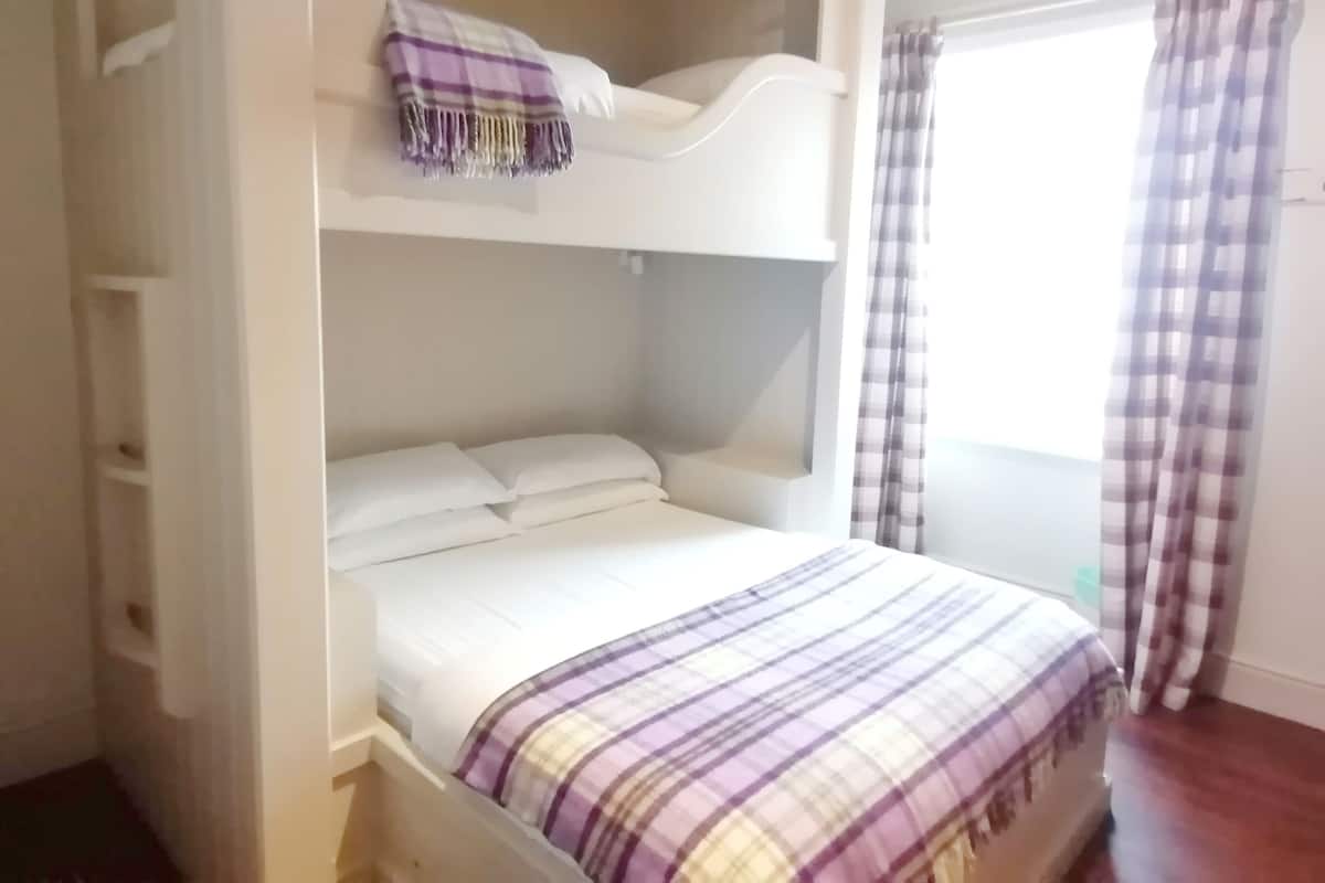 A bunk bed with a purple and white checkered blanket, white pillows, and a white headboard.