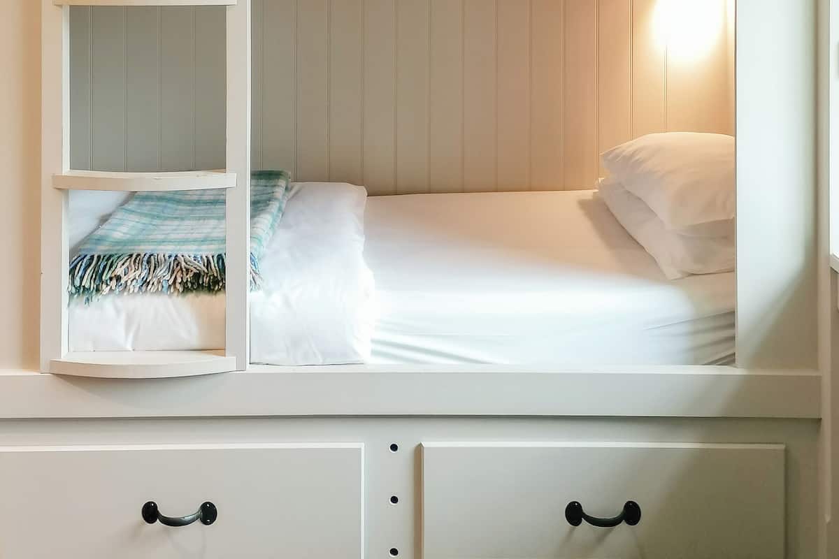 A bunk bed with a headboard, a bedside table, and a lamp.