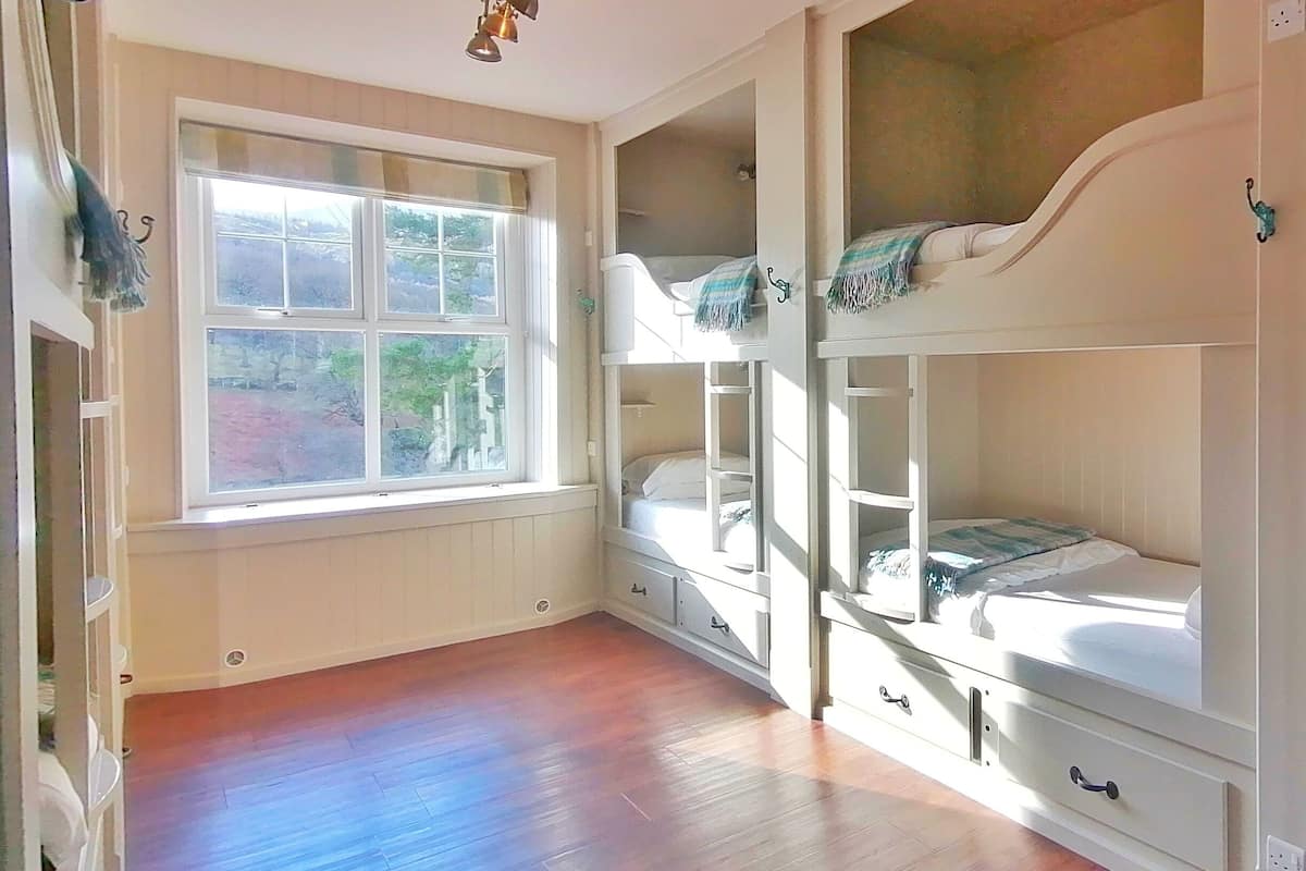 A room with bunk beds, a window with a view, and a ceiling light fixture.
