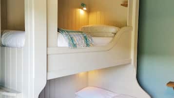 A bunk bed with a lower bunk and a top bunk, both with white bedding. There is a small shelf above the top bunk and a wall-mounted light fixture.