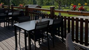 An outdoor patio with tables and chairs, covered by large umbrellas, and surrounded by a wooden deck with flower planters. - Borgsjö Strand (Erikslund)