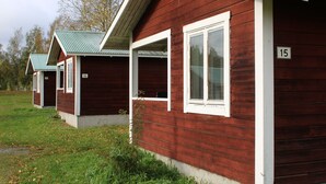 A row of red wooden cabins with white trim and numbered windows, set in a grassy area with trees in the background. - Borgsjö Strand (Erikslund)