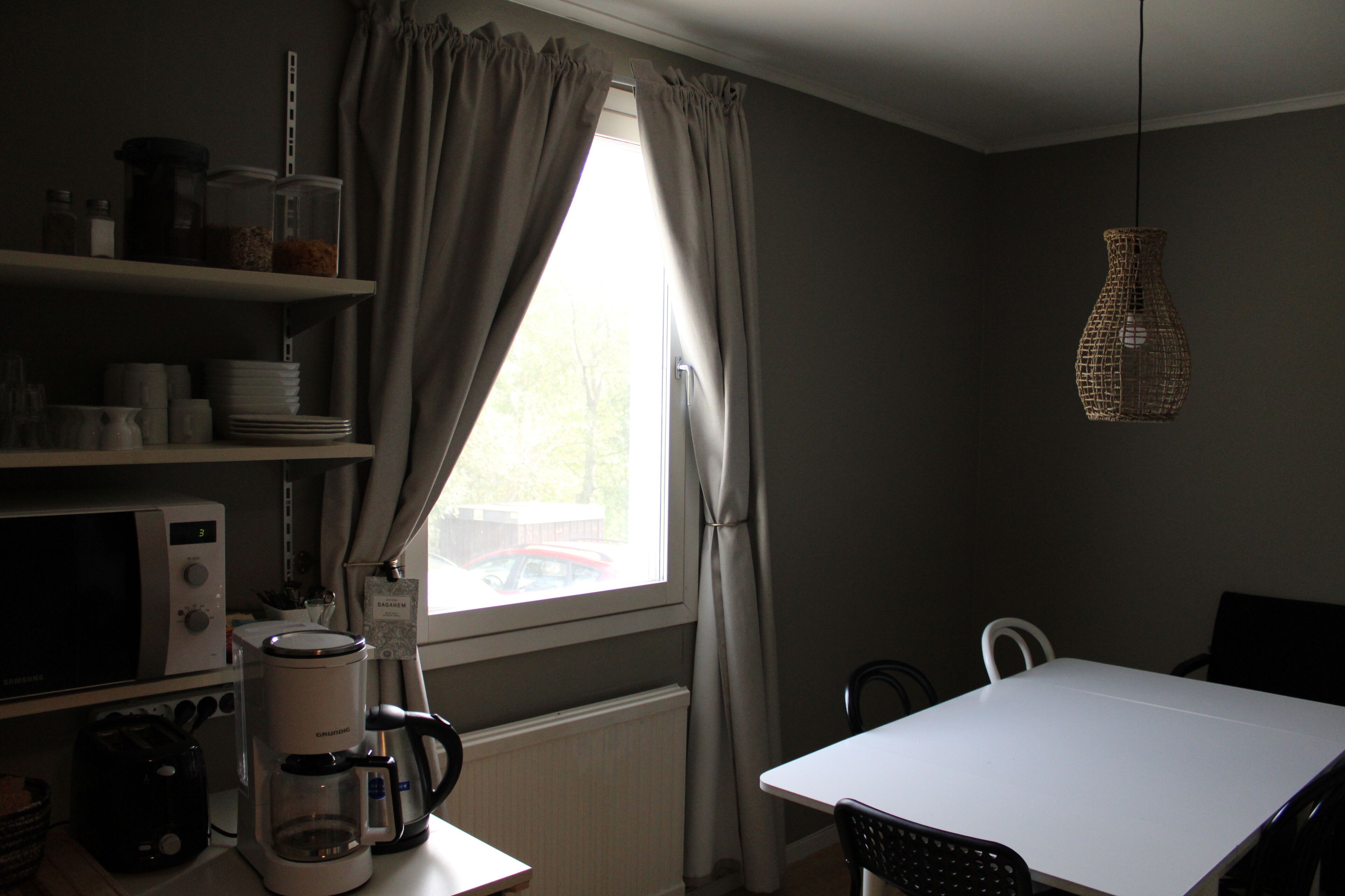 A kitchen with a white table and chairs, a hanging light fixture, and a window with curtains.