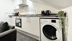 Ett kompakt kök med inbyggd tvättmaskin, mikrovågsugn och kaffebryggare.