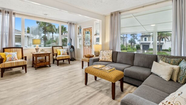A spacious living room with a large gray sectional sofa, two armchairs, and a coffee table. The room has large windows offering a view of palm trees and buildings outside. - 1267 S Fletcher ~ 4 BR House, Walk to the Beach! (Fernandina Beach)