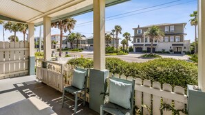 A covered porch with chairs and a white picket fence, overlooking a street with houses and palm trees. - 1267 S Fletcher ~ 4 BR House, Walk to the Beach! (Fernandina Beach)