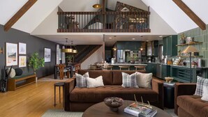 A spacious living area with a brown sofa, a coffee table, and a staircase leading to a loft. - Hidden Homestead: 5 acres, Luxe Cabin, Sauna, Dome, Gym (Bailey)