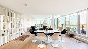 A modern dining area with a round table, white chairs, and a bookshelf. - Riverside Luxury with Iconic Views (London)