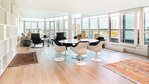 A modern dining area with a round table, black and white chairs, and large windows offering a city view. - Riverside Luxury with Iconic Views (London)