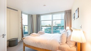 A hotel room with a large bed, a view of the city, and a balcony with a railing. - Riverside Luxury with Iconic Views (London)
