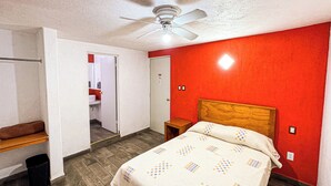 A bedroom with a bed, a wooden headboard, a ceiling fan, a red wall, and a door leading to a bathroom. - Hotel Montecarlo (San Luis Potosí)
