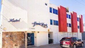 A hotel named "Monte Carlo" with a red and white facade, a parking area, and a red SUV parked in front. - Hotel Montecarlo (San Luis Potosí)