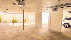 An indoor parking garage with concrete pillars, yellow parking lines, and a white car parked in the background. - Hotel Montecarlo (San Luis Potosí)