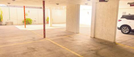 An indoor parking garage with concrete pillars, yellow parking lines, and a white car parked in the background.