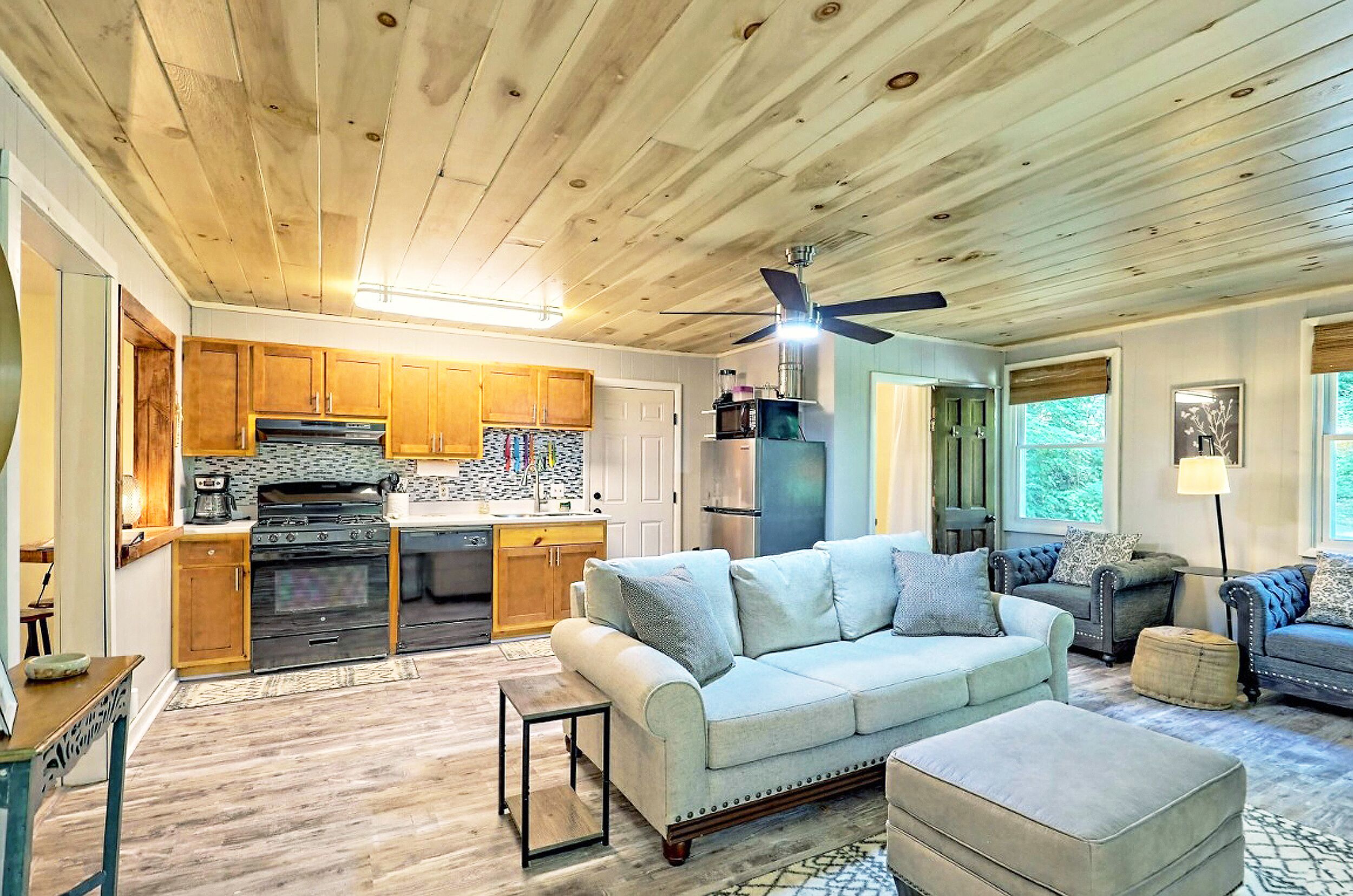 A spacious living area with a sofa, ottoman, and a coffee table. A kitchen with wooden cabinets and appliances is visible in the background.