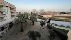 A courtyard with palm trees, a small bridge, and a river. - Apartment lake salonique (Le Grau-du-Roi)