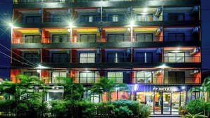 Ein mehrstöckiges Hotel mit Balkonen, einem Restaurant im Erdgeschoss und einer gut beleuchteten Fassade.
