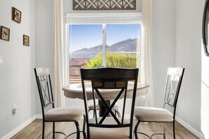 Uma área de refeições com mesa e cadeiras, uma janela com vista para montanhas e um objeto decorativo na parede.