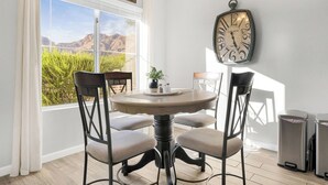 A dining area with a round table, four chairs, a wall clock, and a view of mountains through a large window. - Charming, Clean, Condo with 24 Hour_Gated Access, Spectacular Catalina Mtn Views (Tucson)