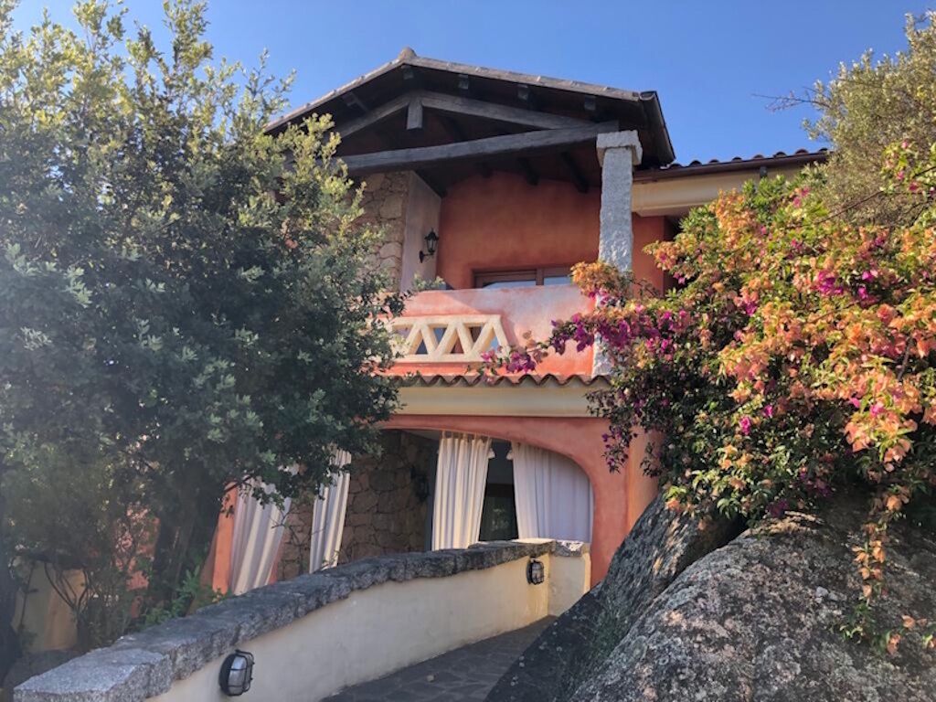 A two-story building with a balcony, stone walls, and flowering plants.