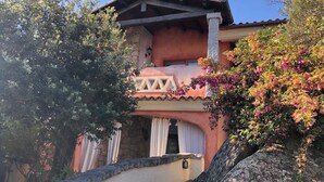 Un edificio a due piani con un balcone, pareti in pietra e piante fiorite.