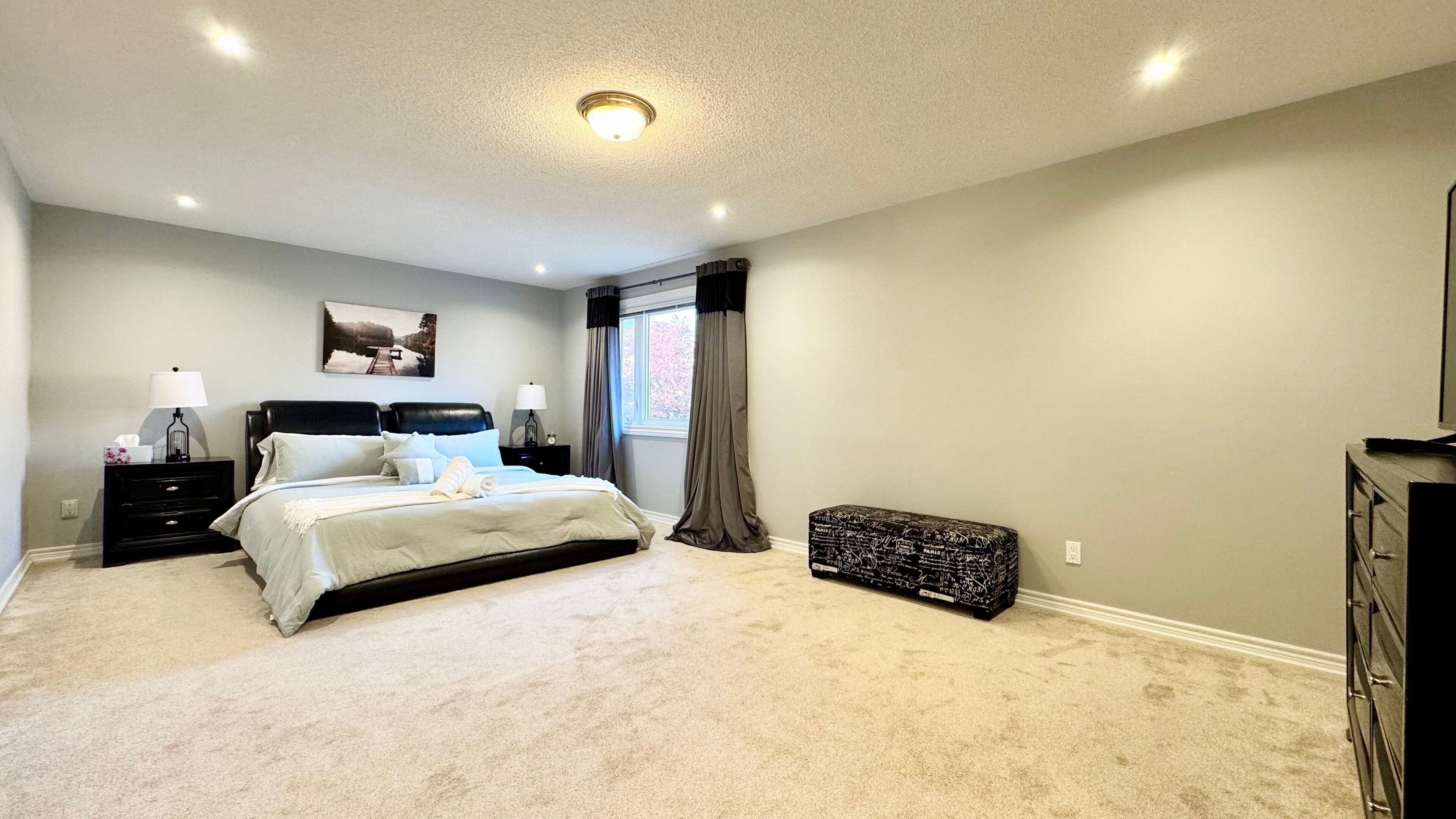 Une chambre à coucher avec un lit, des tables de chevet, une commode et une fenêtre avec des rideaux.