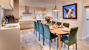 A modern dining area with a wooden table, green upholstered chairs, pendant lighting, and a framed picture on the wall. - Aysgarth Nook by Luxury Travel Emporium (Aysgarth)