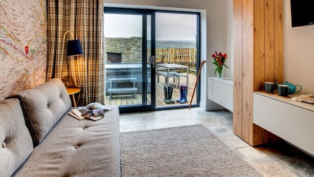A modern living room with a sofa, a map on the wall, a sliding glass door leading to an outdoor area with a table and chairs, and a wooden cabinet with a TV. - Aysgarth Nook by Luxury Travel Emporium (Aysgarth)