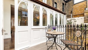 Une terrasse couverte avec une table ronde et deux chaises, une porte blanche et un mur en briques.