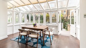 Une véranda avec une table et des chaises en bois, de grandes fenêtres et une vue sur le jardin.