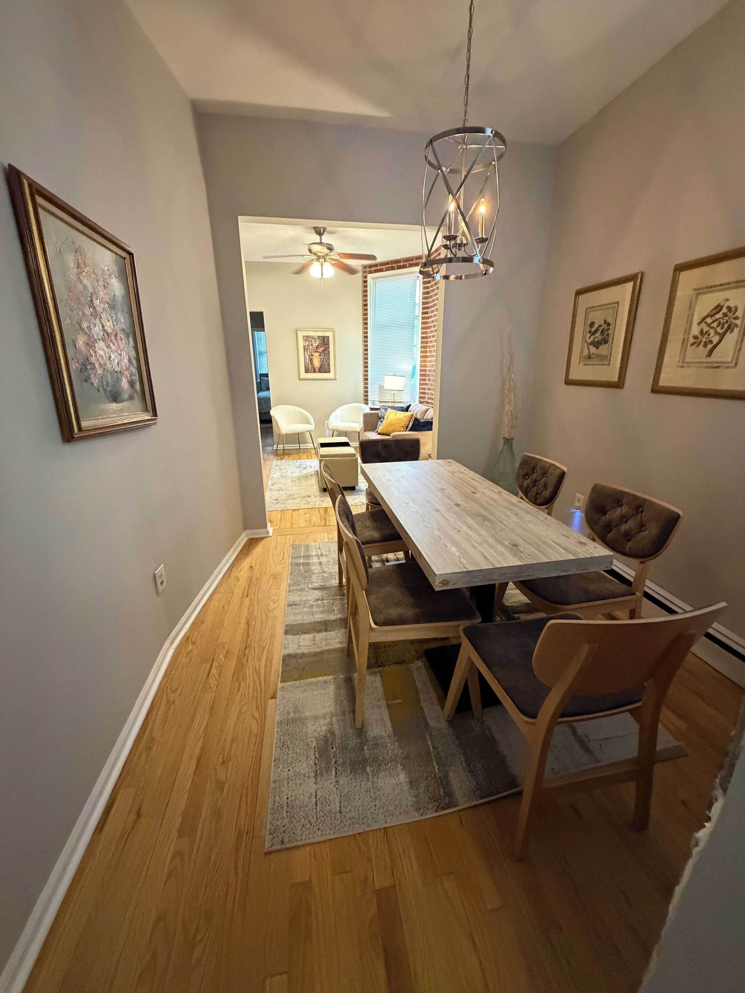 A dining area with a wooden table and chairs, a chandelier, and a view into the living room.